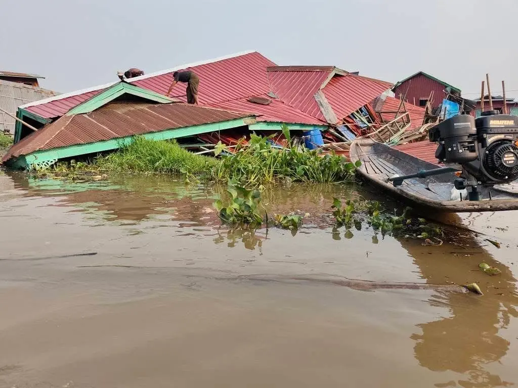 Men repair the roof of a house collapsed into the water at Inle Lake