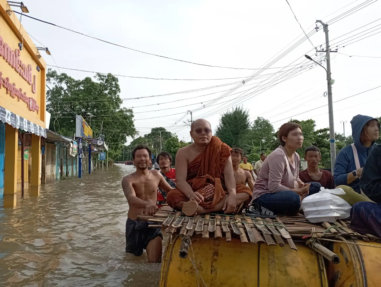 A monk and residents cross a flooded Mandalay street on a raft floated on oil drums, pushed by a man wading chest-deep