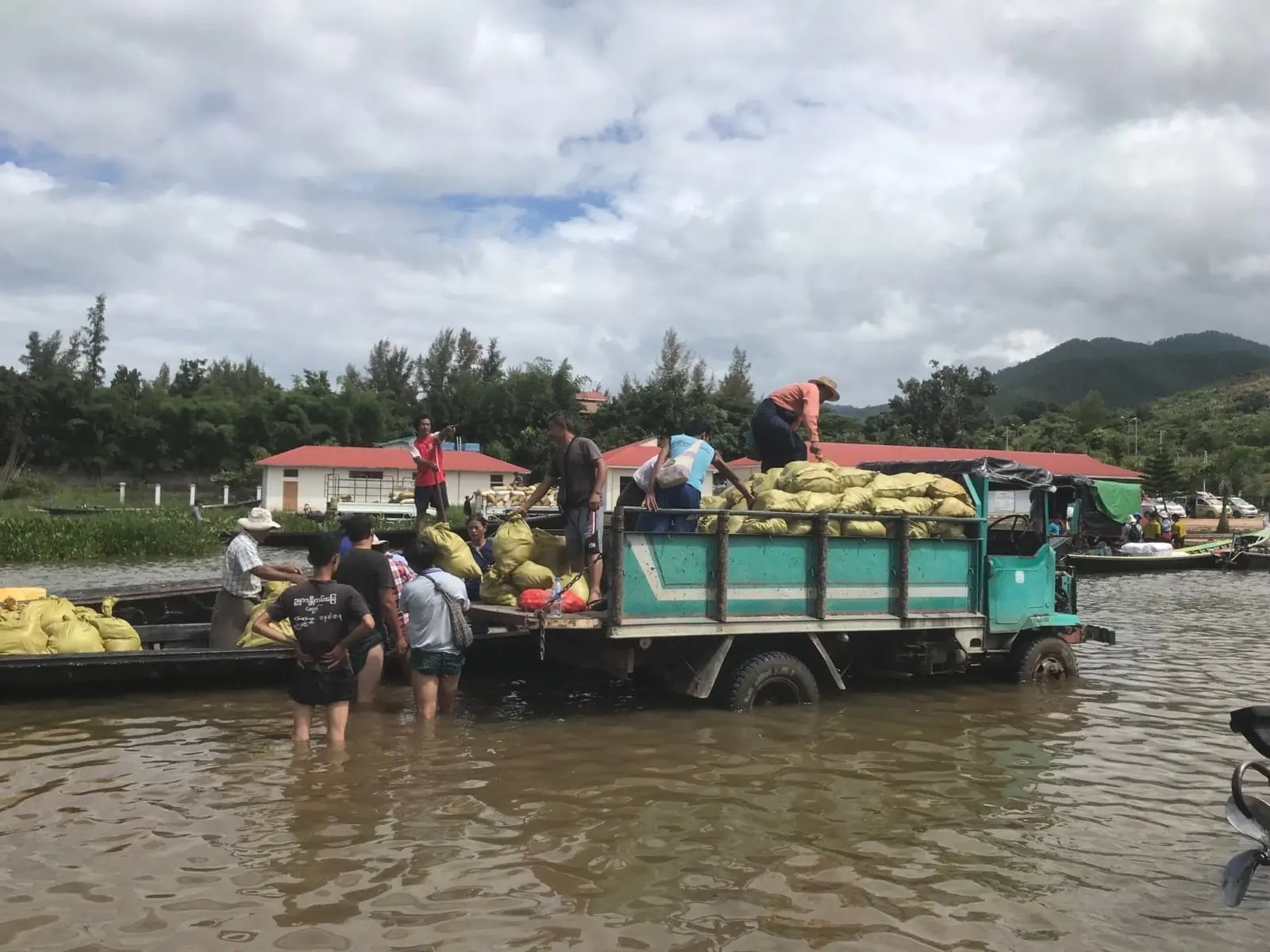Volunteers wade through floodwater to unload sacks of relief supplies from a truck onto boats