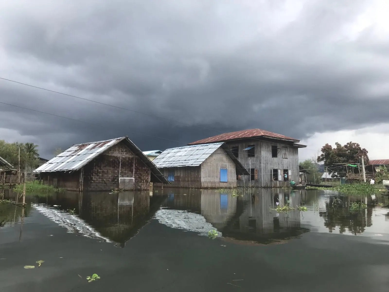 Village houses standing in floodwater under a storm sky