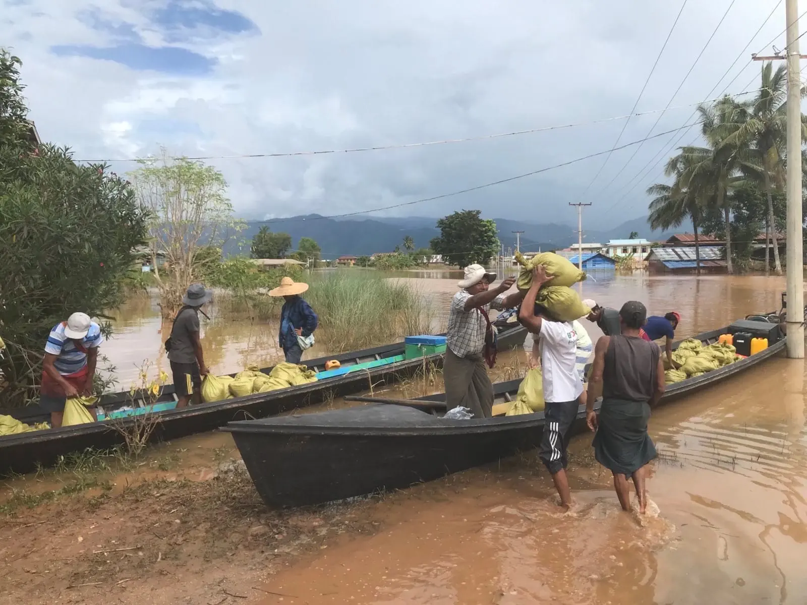 Volunteers carry relief sacks on their shoulders from boats onto a flooded road