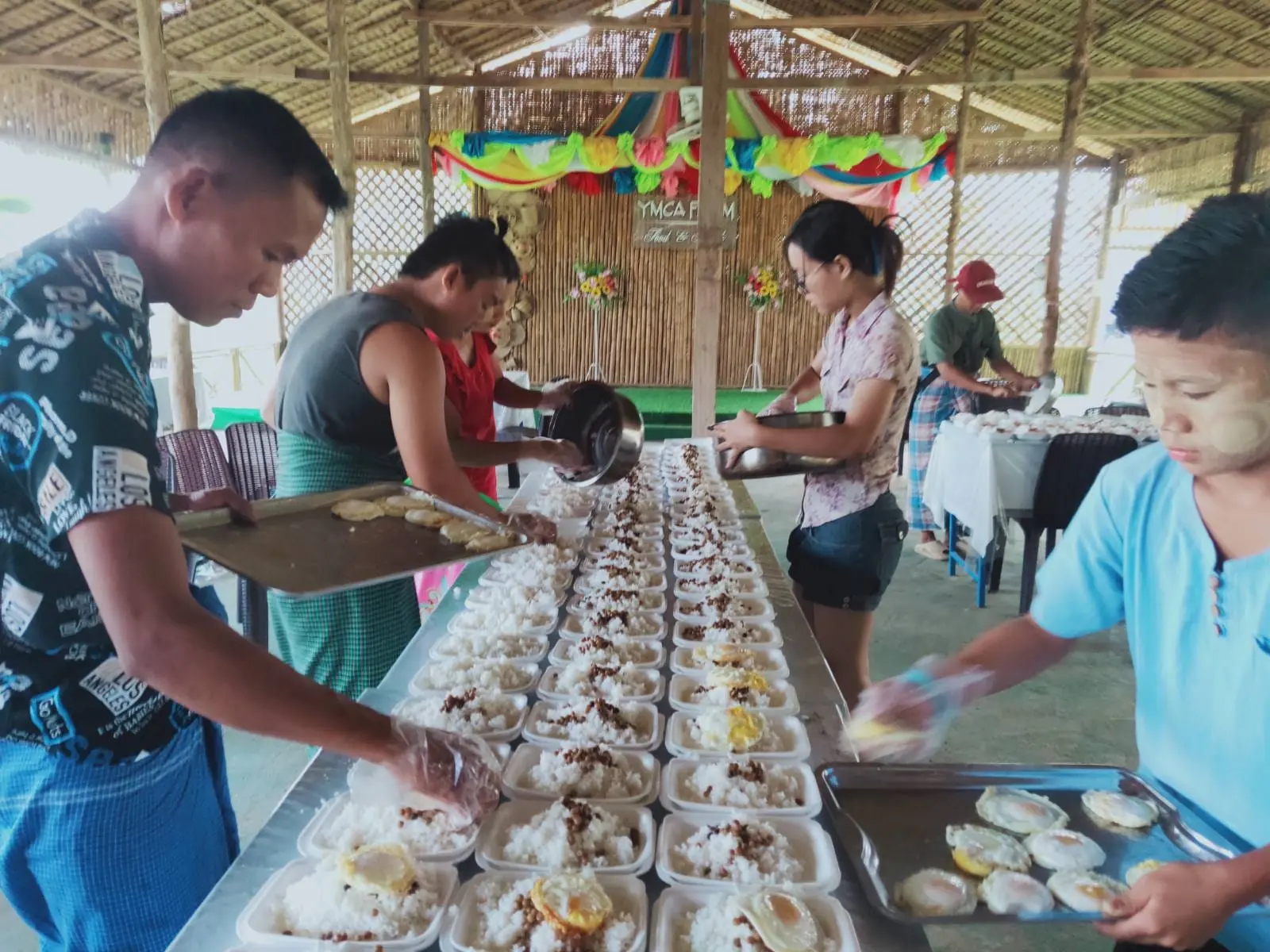 Volunteers fill rows of meal boxes with rice and eggs for donation to hospitals